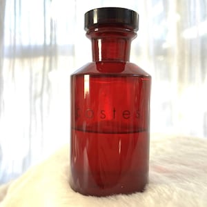 May include: A red glass bottle with a black cap. The bottle has the word "costes" printed on the front. The bottle is filled with a red liquid.