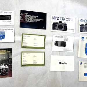Puede incluir: Una colección de manuales y accesorios para cámaras Minolta, incluyendo Auto Winder D, XD-11 y Auto Electroflash 360PX. Los manuales presentan ilustraciones y texto en blanco y negro, con el logotipo de Minolta.