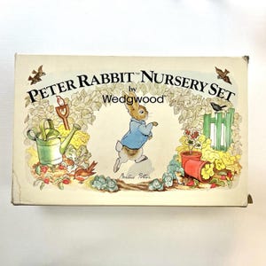 May include: A vintage Peter Rabbit Nursery Set box by Wedgwood. The box features illustrations of Peter Rabbit in a blue jacket, a watering can, and garden elements. The box is cream-coloured with the text "Peter Rabbit Nursery Set".