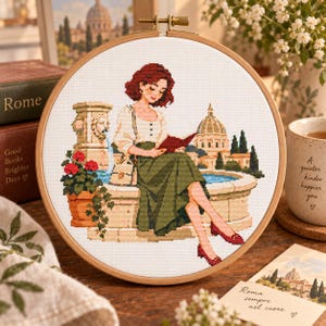 May include: A circular wooden embroidery hoop containing a cross-stitch pattern of a person with short auburn hair reading a book whilst sitting on a stone fountain in Rome. The scene includes a lion-head fountain, red flowers, and a domed building.