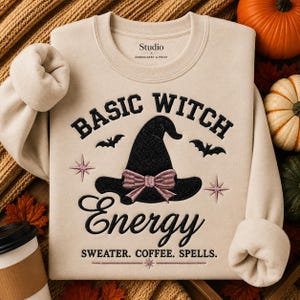 May include: A beige crewneck sweatshirt featuring black embroidered text that reads BASIC WITCH ENERGY and SWETER. COFFEE. SPELLS. The design includes a black witch hat with a pink bow, two black bats, and two pink starburst icons.