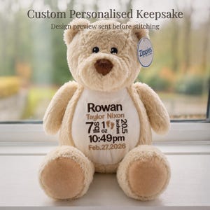 May include: A beige plush teddy bear with a brown nose and embroidered details. The bear has a white patch on its chest with the name "Rowan", birth details: 7 lbs 1 oz, 20.5 inches, 10:49 pm, Feb.27,2026. The tag reads "Zippies".