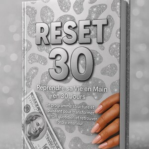 Peut inclure: Un livre intitulé "RESET 30" avec des lettres argentées et un fond scintillant. La couverture présente également du texte en français et un billet de 100 dollars américains. Une main avec des ongles manucurés est visible.