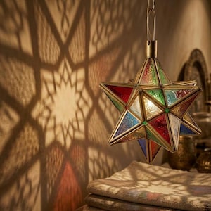 May include: A hanging star-shaped lantern with colorful stained glass panels in red, green, blue, and yellow. The lantern is suspended by a gold chain, casting intricate geometric shadows on the wall and a stack of folded towels.