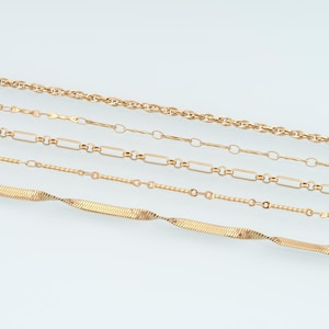 May include: A collection of four gold-toned metal chains arranged horizontally. The top chain is a twisted rope style, followed by a delicate link chain, a rectangular link chain, and a flat, flexible herringbone chain at the bottom.