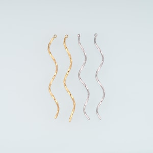 Può includere: Quattro componenti per orecchini in metallo lunghi, sottili e ondulati disposti verticalmente. Due sono color oro e due color argento. Ogni pezzo presenta un design a spirale continuo e fluido con un piccolo occhiello in alto per l'aggancio.