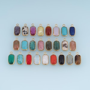 May include: A collection of twenty-four rectangular jewellery charms, each featuring a faceted gemstone set in a gold-toned metal frame with a small circular loop at the top. The charms display a variety of colours including red, blue, green, pink, black, and white, with some showing natural stone patterns.