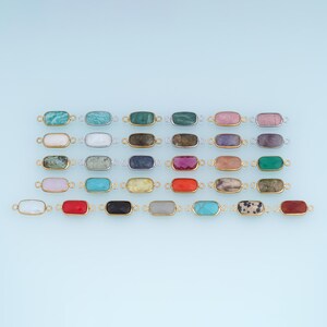 May include: A collection of rectangular gemstone connectors arranged in rows. Each stone is set in a metallic frame with small loops on both sides. The stones feature various colors including turquoise, pink, white, black, red, and patterned textures.