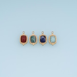 Op de afbeelding: Vier rechthoekige sieradenbedels met goudkleurige metalen frames en gefacetteerde stenen in rood, groen, donkerblauw en lichtblauw. Elke bedel heeft een kleine ronde lus aan de bovenkant voor bevestiging en is voorzien van een gepolijste afwerking.