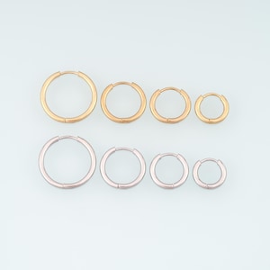 Può includere: Una collezione di otto orecchini a cerchio disposti su due file. La fila superiore presenta quattro cerchi color oro di dimensioni graduate, mentre la fila inferiore mostra quattro cerchi color argento abbinati di dimensioni graduate.