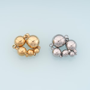 May include: Two sets of spherical jewellery clasps. One set is gold-toned, and the other is silver-toned. Each clasp is composed of multiple spheres of varying sizes, clustered together. The clasps are on a light blue background.