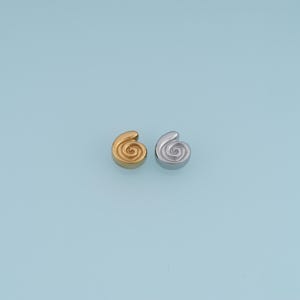 以下が含まれることがあります： 螺旋状の貝殻の形をした2つの小さな金属製チャーム。1つは光沢のあるゴールドトーン、もう1つは光沢のあるシルバートーンで仕上げられています。各チャームには、中心から外側に向かって広がる隆起した同心円状の渦巻き模様が施されています。