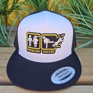 May include: A black and white snapback hat with a light blue and white front panel. The hat features a patch with stick figures and the text "PROBLEM SOLVED". The hat has a curved brim and a mesh back.