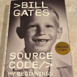 May include: A hardcover book titled "SOURCE CODE/> MY BEGINNINGS" by Bill Gates. The cover features a black and white photo of a young Bill Gates. A gold sticker on the cover reads "SIGNED COPY".