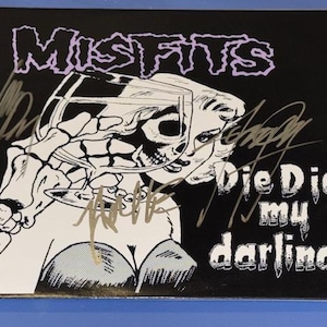 May include: Black album cover featuring the band name "Misfits" in purple, and the phrase "Die Die my darling" in white. The cover art depicts a woman's face with a skull overlay, holding a glass. Several signatures are visible.