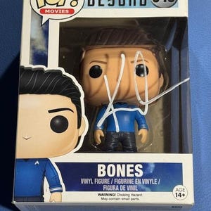Könnte beinhalten: Eine Star Trek Beyond "Bones" Vinylfigur in einer Pop! Movies Box. Die Figur trägt eine blaue und schwarze Uniform. Die Box hat das Pop! Movies Logo und die Nummer 349. Die Box ist weiß mit blauen Akzenten und dem Text "BONES".