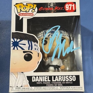 Può includere: Una statuetta in vinile Funko Pop! di Daniel LaRusso della serie televisiva Cobra Kai. La statuetta è in una vetrina di plastica trasparente. La scatola presenta il logo Pop! Television e il numero 971. La statuetta è firmata con un pennarello blu.