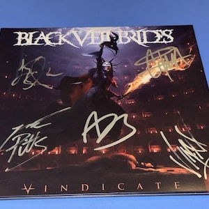 May include: A square music album cover featuring the band name Black Veil Brides and the word Vindicate. The artwork depicts a dark, hooded figure holding a flaming sword in a stone arena. The cover is signed with five distinct gold ink autographs.