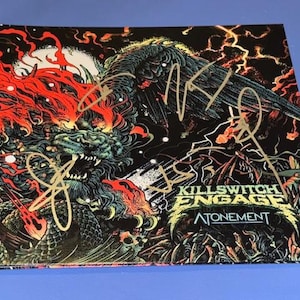 Può includere: Copertina dell'album "Atonement" dei Killswitch Engage con un'illustrazione di drago con sfumature rosse e verdi. La copertina dell'album è firmata con inchiostro dorato. Il nome della band e il titolo dell'album sono visibili.