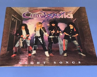 May include: Album cover for Cinderella's "Night Songs" featuring four band members in rock attire. The band name is in a purple, stylized font. The album title is at the bottom. An autograph is visible.