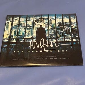 May include: The Dark Knight original motion picture soundtrack CD. The cover features a silhouette of Batman against a cityscape backdrop. The CD case has the film's title and composer credits.