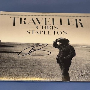 Könnte beinhalten: Albumcover für "Traveller" von Chris Stapleton, mit einem Schwarz-Weiß-Bild eines Mannes mit Hut, der über ein Feld blickt. Der Albumtitel und der Künstlername sind oben aufgedruckt. Eine Unterschrift ist sichtbar.