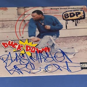 May include: Album cover for "Duck Down" by Boogie Down Productions. The cover shows a man in a blue shirt and jeans, with graffiti-style text and the words "Duck Down" in a starburst. The BDP logo is also visible.