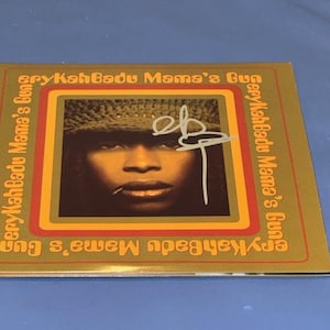 May include: A CD case for Erykah Badu's album "Mama's Gun." The cover shows a portrait of Erykah Badu with a signature. The album title and artist's name are printed in a gold font around the border.