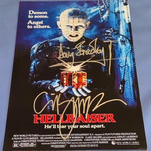 May include: A movie poster for the horror film Hellraiser. The poster features a central figure with a pale face and pins, holding a puzzle box. The title "Hellraiser" is in red, with the tagline "He'll tear your soul apart."