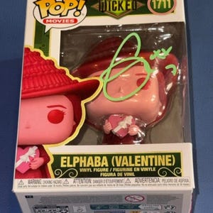 May include: A Funko Pop Movies Wicked Elphaba Valentine vinyl figure in its original packaging. The box features the number 1711, a green autograph on the plastic window, and an illustration of the character wearing a red hat and holding a heart.