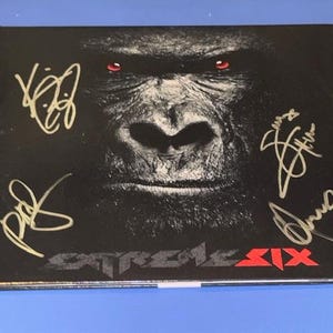 Op de afbeelding: Een zwarte albumhoes met een gorilla's gezicht met rode ogen en meerdere gouden handtekeningen. De bandnaam "Stroke Six" staat in het rood onderaan.