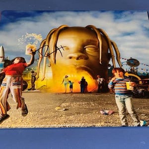 Puede incluir: Una portada de álbum firmada con una gran cabeza dorada con los ojos cerrados. La obra de arte representa una escena surrealista con figuras, un cohete y un ambiente de carnaval. La firma es con tinta negra.