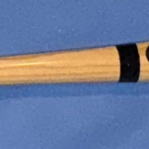 Pode incluir: Um bastão de beisebol de madeira clara. Possui uma faixa preta perto da pega, um logotipo da Rawlings e uma assinatura. O bastão está sobre um fundo azul.