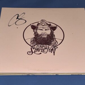 Könnte beinhalten: Ein hellrosa Albumcover mit einem braunen Porträt von Chris Stapleton mit Hut und Bart, umrandet von einer braunen Kontur. Der Name "Chris Stapleton" steht unter dem Porträt. Das Cover ist mit einem schwarzen Marker signiert.