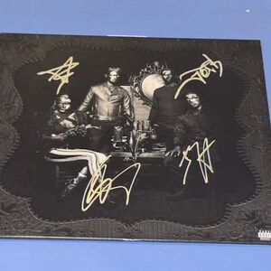 May include: A black album cover featuring a group of people in a dark setting, with gold signatures. The cover has an ornate border and a small parental advisory label.