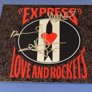 Puede incluir: Una portada de álbum cuadrada con las palabras "EXPRESS" y "LOVE AND ROCKETS" en rojo. El centro presenta un diseño en blanco y negro con un corazón rojo y firmas. El fondo tiene un patrón de rosas oscuras.