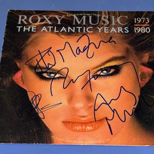 May include: Roxy Music album cover, featuring a woman's face with bold makeup and signatures. The album title, "The Atlantic Years 1973-1980," is printed at the top. The cover has a vintage aesthetic.