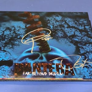 May include: A CD case featuring the album art for Pantera's "Far Beyond Driven." The cover art is predominantly blue with a skull-like image and a brown, spine-like structure. The band's name and album title are visible.