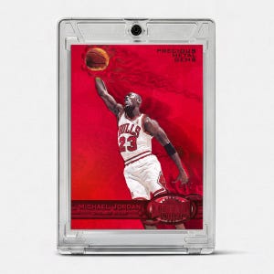 May include: A Michael Jordan Precious Metal Gems trading card encased in a clear protective plastic holder. The card features a red background with a basketball player in a white Chicago Bulls jersey with the number 23, reaching for a basketball.