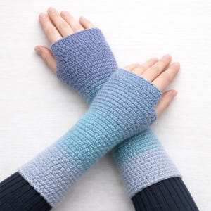 May include: Crocheted fingerless gloves in shades of blue, from periwinkle to aqua. The gloves are handmade with a textured stitch and cover the hands and forearms. The sleeves are approximately 12 inches long.