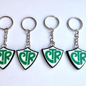 May include: Four keychains with a shield-shaped pendant. Each pendant has a white background with the letters "CTR" in green, outlined in black. The keychains have silver-colored key rings and chains.