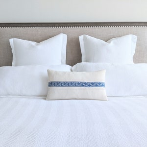 May include: A white bed with a gray headboard and white bedding. The bed has two white pillows and a decorative pillow with a blue stripe.
