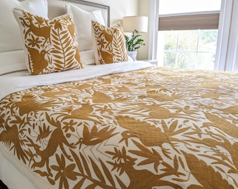 May include: A white bed with a mustard yellow embroidered quilt featuring a floral and bird design. The bed has white pillows with mustard yellow embroidered covers.