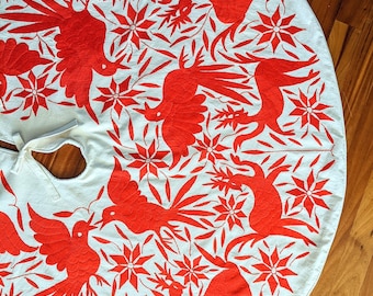 Pode incluir: Uma toalha de mesa circular branca com um desenho bordado vermelho de pássaros e flores estilizados. A toalha de mesa é perfeita para uma ocasião festiva.