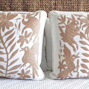Puede incluir: Dos almohadas blancas con diseños florales y de pájaros bordados en marrón. Las almohadas están sobre una colcha blanca.