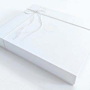 May include: A white gift box tied with a white string bow. The box has a gold sticker with the text "MADE IN NY" on it.