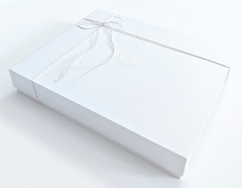 May include: A white gift box tied with a white string bow. The box has a gold sticker with the text "MADE IN NY" on it.