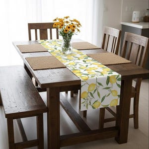 May include: A rustic wooden dining table set with a bench and chairs. The table is adorned with a lemon-patterned table runner and placemats. A vase of yellow flowers sits in the center, creating a bright and inviting dining space.