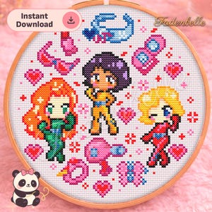 Può includere: Un telaio da ricamo a punto croce con tre personaggi dei cartoni animati in abiti colorati, circondati da cuori e altri elementi decorativi. Il testo "Instant Download" è visibile. Il telaio è posto su uno sfondo rosa.