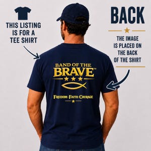 May include: A navy blue t-shirt featuring a gold graphic on the back. The text reads BAND OF THE BRAVE with three stars, a fish symbol, and the words FREEDOM FAITH COURAGE. Additional text indicates this listing is for a tee shirt.
